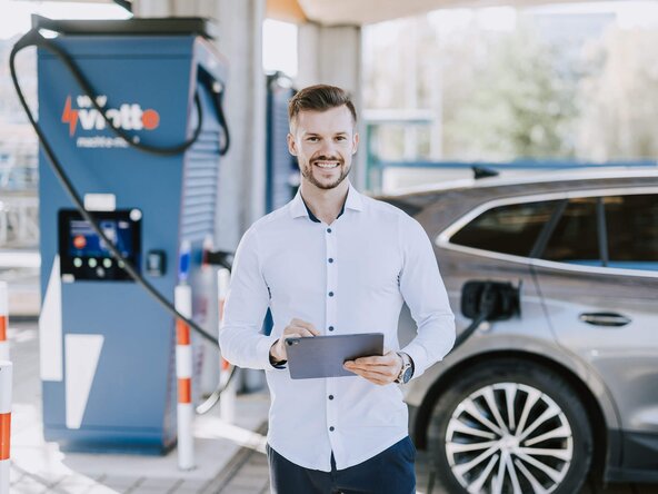 Techniker steht mit Tablet vor Schnelllader, der ein Fahrzeug lädt