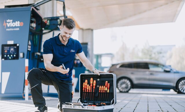 Techniker sucht sein Werkzeug in einem Werkzeugkoffer vor dem Schnelllader