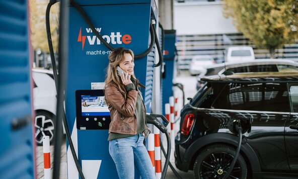 Junge Frau telefoniert, während ihr Fahrzeug am Schnelllader auflädt